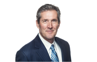 Brian Pallister devant un arrière-plan blanc, porte une chemise blanche sous un manteau bleu marin avec une cravate bleu pâle.