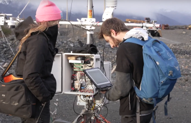 two students stand in front of a weather monitoring station