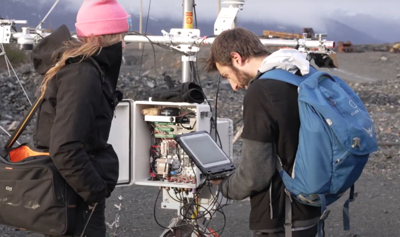 two students stand in front of a weather monitoring station