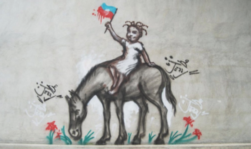 A graffiti painting shows a young Haitian girl on the back of a horse. She is holding the flag of Haiti.