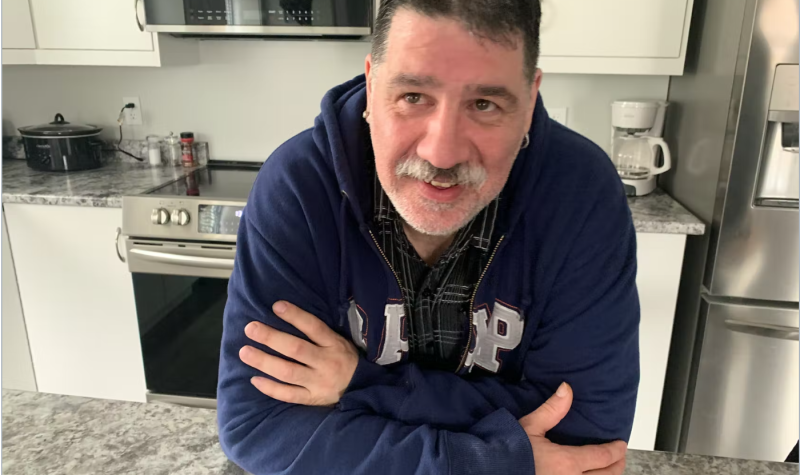 Craig Boutilier is wearing a navy blue sweater and smiling over the table of his apartment kitchen.