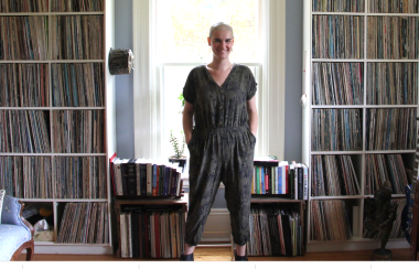 Sarah McInnis is standing in her office behind shelves of books, cds, and near guitars.