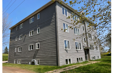 A square, three story building with basement windows, in beige siding.