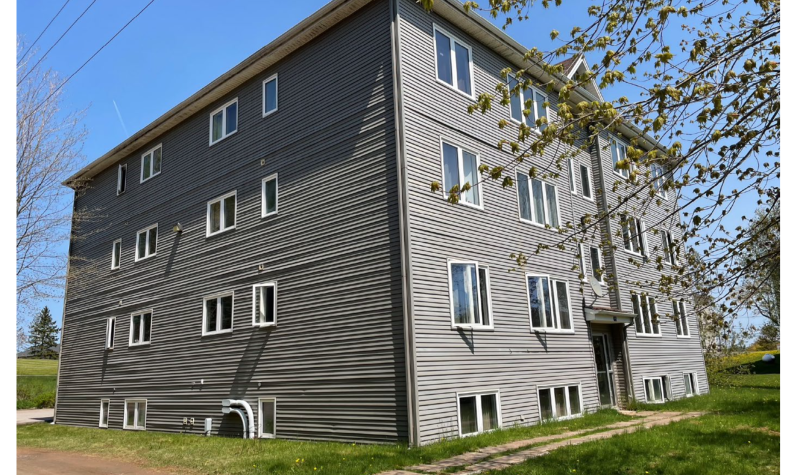 A square, three story building with basement windows, in beige siding.