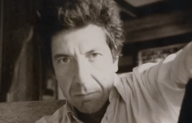 A young Leonard Cohen looks into the camera in a black and white photograph.