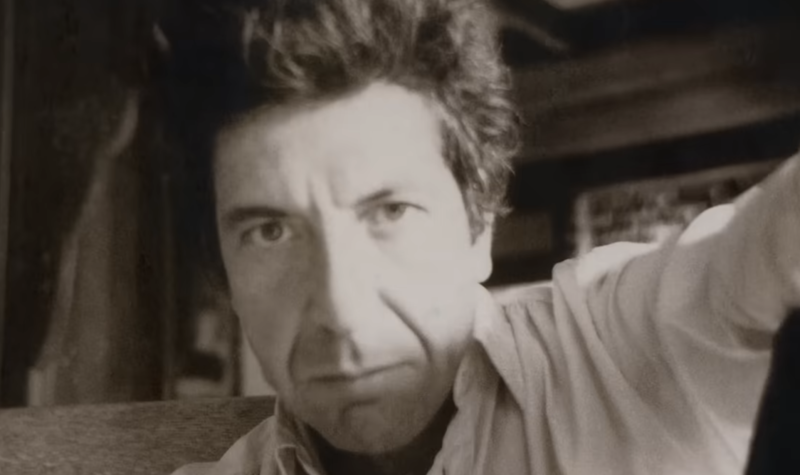 A young Leonard Cohen looks into the camera in a black and white photograph.