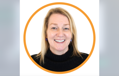 Portrait photo of climate change specialist Nancy Anningson wearing black, smiling. She has blonde hair, and is standing in front of a plain white background.