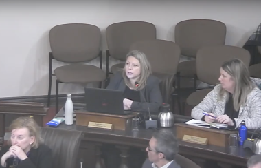 Lanie Hurdle, chief administrative officer for the City of Kingston, is speaking at city council in chambers. One other woman sits to her left, with other councillors sitting in the row below.