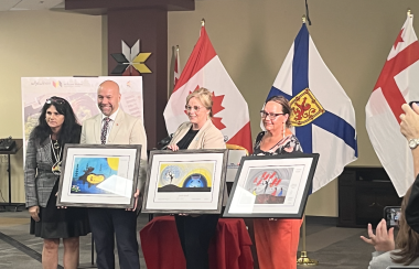 Pam Glode Desrochers presents Indigenous artwork to Andy Fillmore, Karla MacFarlane and Chief Annie Bernard-Daisley who hold up the artwork in front of new building rendering and Canadian, Nova Scotia and Mi'kmaw flags.