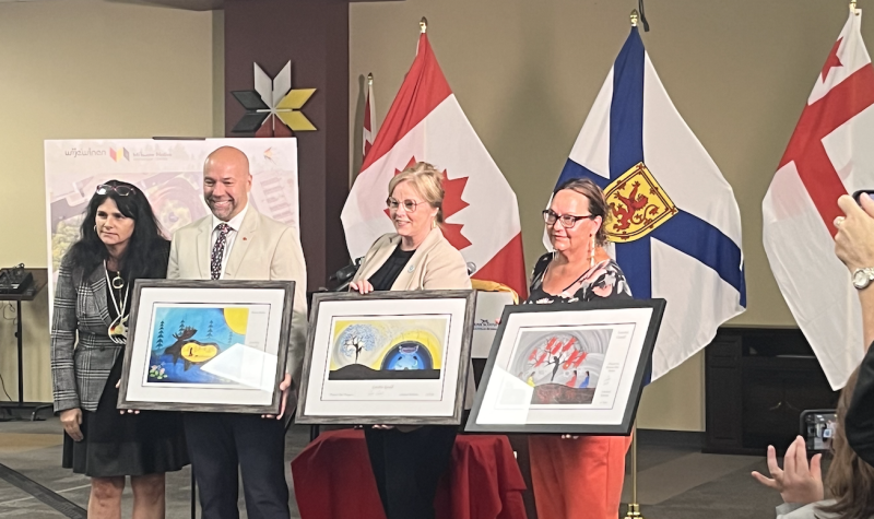 Pam Glode Desrochers presents Indigenous artwork to Andy Fillmore, Karla MacFarlane and Chief Annie Bernard-Daisley who hold up the artwork in front of new building rendering and Canadian, Nova Scotia and Mi'kmaw flags.