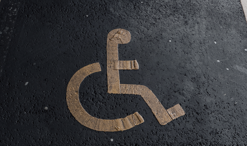 Disabled parking symbol in yellow painted on pavement to mark a disabled parking space