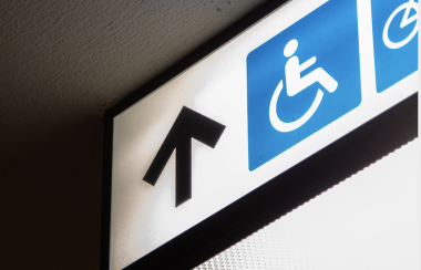 Light up sign hung on a ceiling shows upward arrow, wheelchair and bicycle symbols.