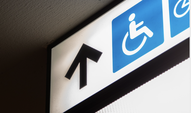 Light up sign hung on a ceiling shows upward arrow, wheelchair and bicycle symbols.