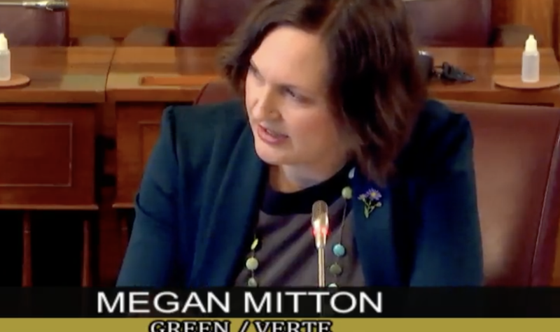 A woman sitting at a desk speaking into a microphone, with overlay reading Megan Mitton, Green, Memramcook-Tantramar