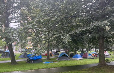 Tents in a park in front of a paved path with trees surrounding them