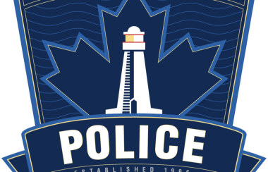 Halifax Regional Police in white with a white lighthouse against a blue badge with a maple leaf and Nova Scotia flag outlined on it.
