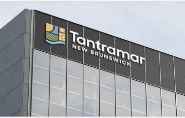 A grey building with a front wall consisting of glass floor to ceiling windows. The top two floors are dark grey with a logo and Tantramar, New Brunswick featured at the top left.