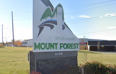 A sunny day in Mount Forest. A sign for Mount Forest sits on a lawn reading 'Simply Explore.'