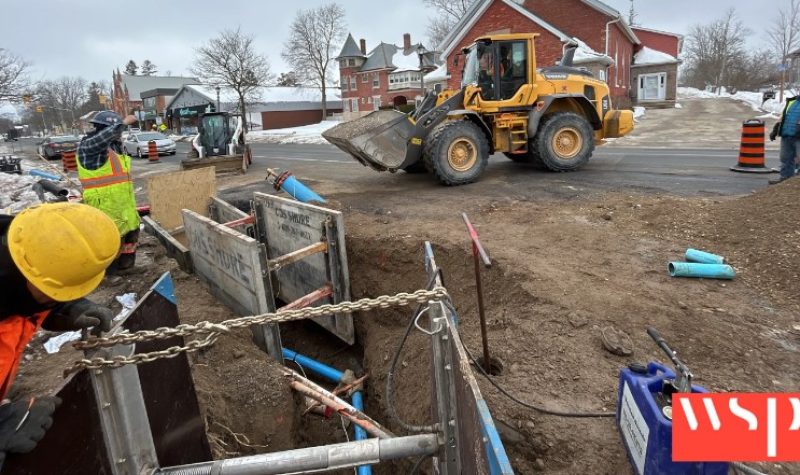 A construction zone with a bulldozer is closed off with traffic cones as people in fluorescent vests work away.