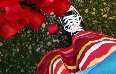 A shot looking down at someone's feet, wearing a red ribbon skirt in front of some roses. Weather looks rainy