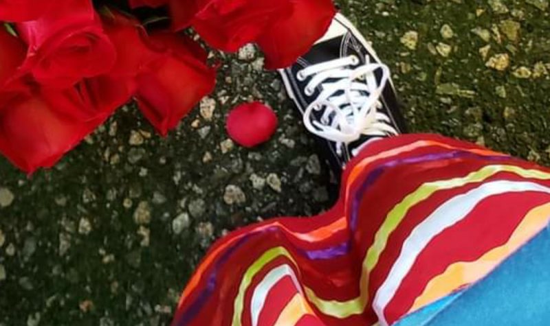 A shot looking down at someone's feet, wearing a red ribbon skirt in front of some roses. Weather looks rainy