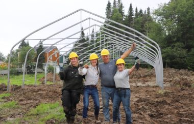 Quatre personnes portant un casque de construction célèbrent, bras levés, devant la structure d'une serre.