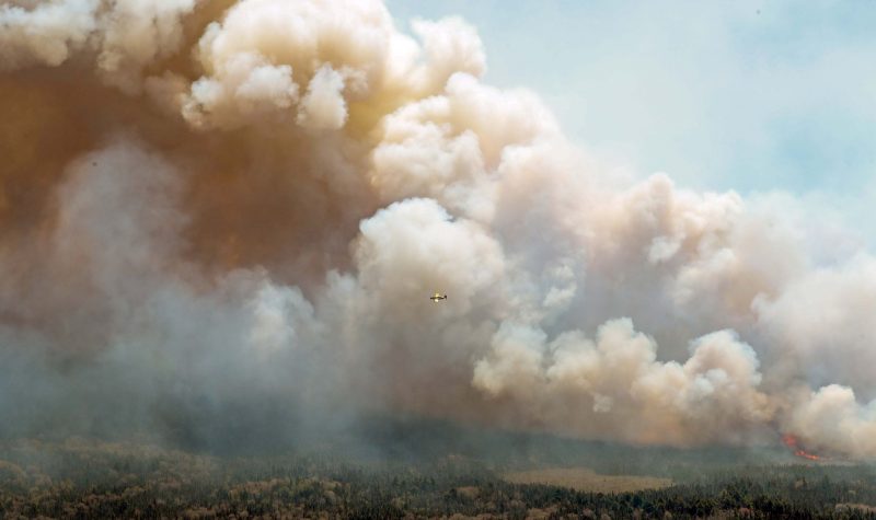 A water bomber flies through the smoke of a forest fire
