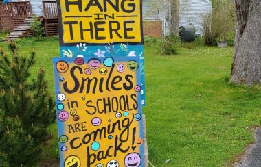Signs posted on a lawn encouraging people to hang in there, smiles are coming back to schools