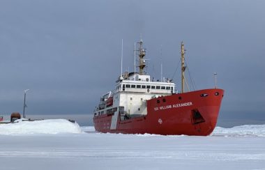 Un navire à la cale rouge aux abords d'un quai. Il semble reposer sur un sol enneigé et glacé.