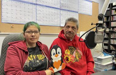 Two people sit a microphone in CKRZ studio with penguin sign.