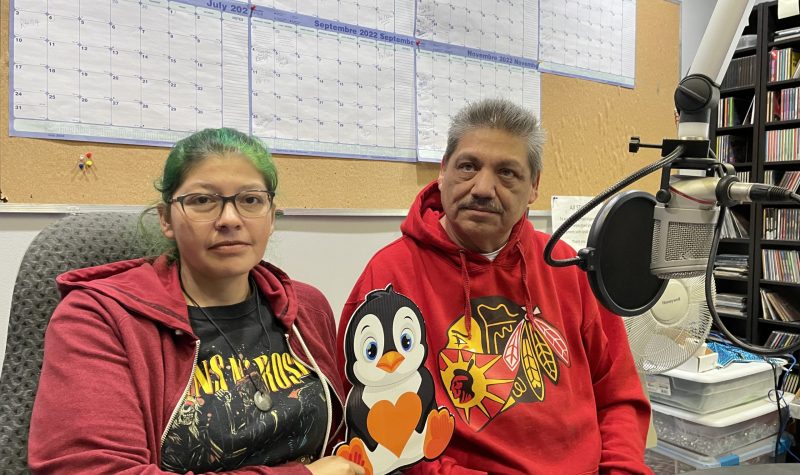 Two people sit a microphone in CKRZ studio with penguin sign.