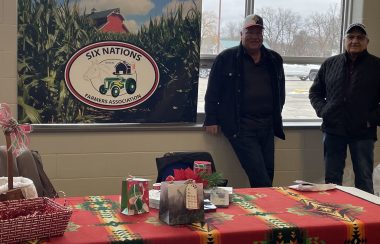 two men stand against window with Farmers sign beside them and table infront draped with blanket and items