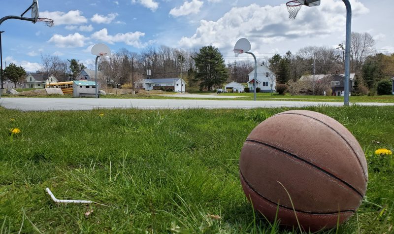 A basketball rests in the grass beside a playground