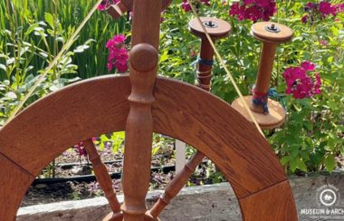 A wooden spinning wheel and flowers coexist in an outdoor garden.