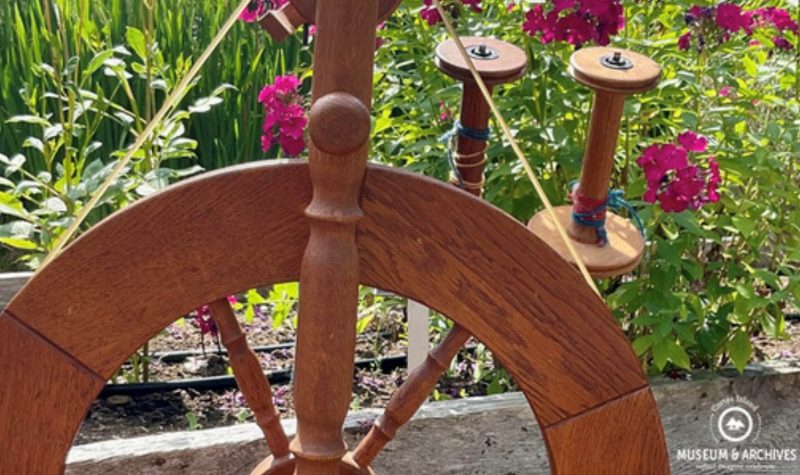 A wooden spinning wheel and flowers coexist in an outdoor garden.