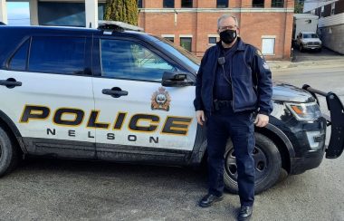 A police officer in mask in front of patrol car