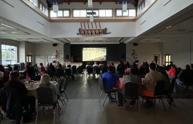 A darkened room full of people sit watching a large screen of the Stanley cup Final at Six Nations