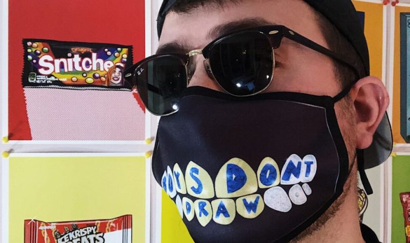 Stefan Perić is standing in front of a wall of his art, wearing a BOYSDONTDRAW face mask and sunglasses.