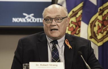 A man sits at a desk speaking through a microphone