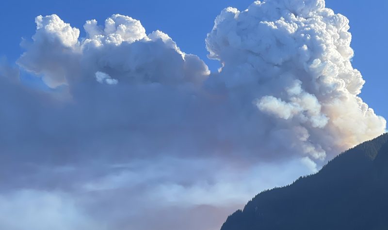 wildfire smoke rises over a mountain.