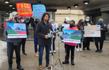 A group of people holdinh up several colourful signs as they stand outside in front of a subway street entrance.