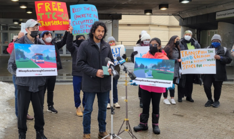 A group of people holdinh up several colourful signs as they stand outside in front of a subway street entrance.