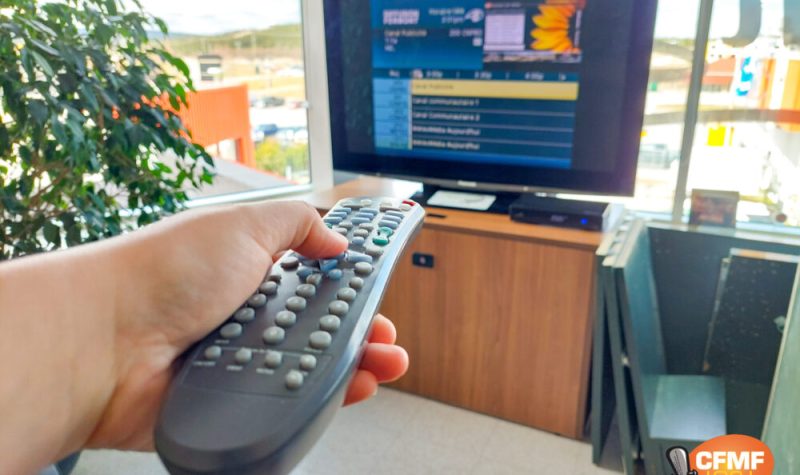 Main tenant une télécommande devant un écran de télévision allumé