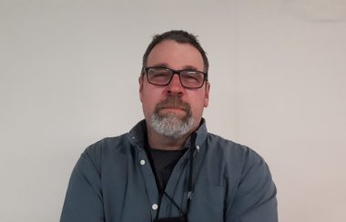 A headshot of Terry Lafleur, wearing a grey collard shirt and glasses in front of a plain background.