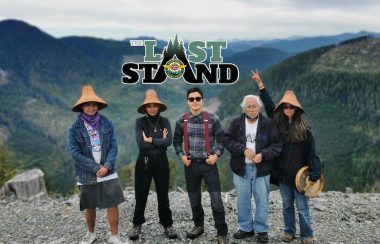 Five Indigenous people stand in front of a green valley