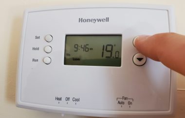 A white Honeywell thermostat on the wall with a finger pressing a button.