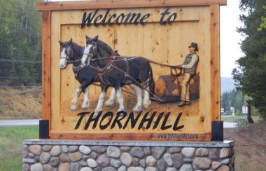A wooden sign that says Welcome to Thornhill with an image of a man in a carriage being pulled by two horses