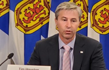 A man sits in front of a row of Nova Scotia flags