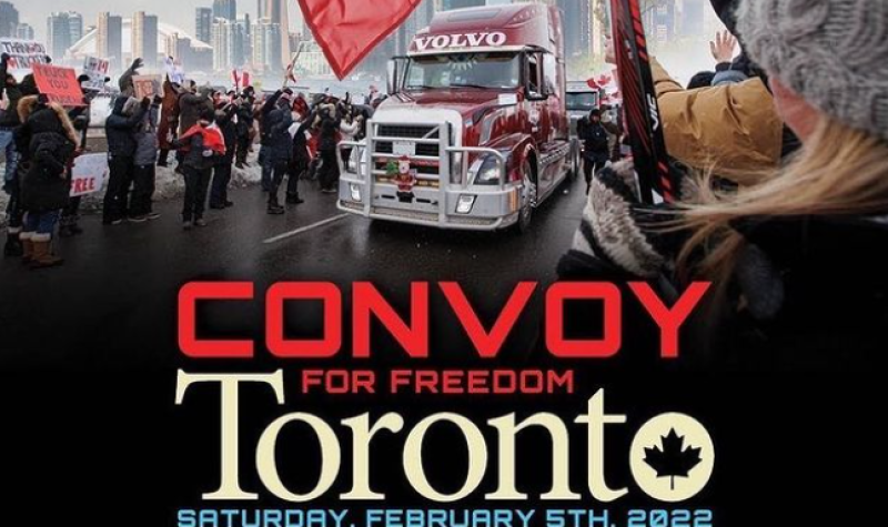 A truck on a road surrounded by a crowd of people holding red and white Canadian flags with buildings in the background.