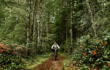 A woman cycling along a trail through the woods on Cortes Island